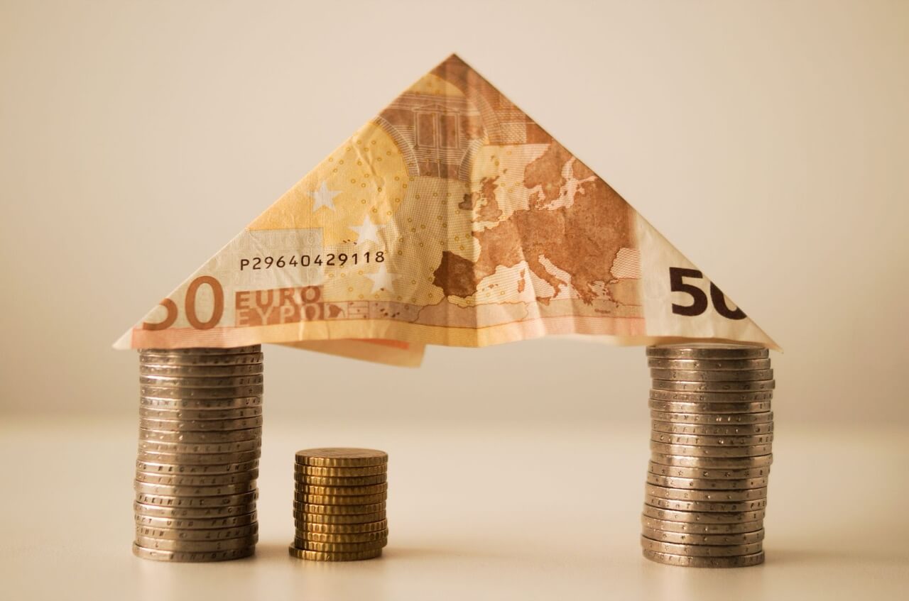 house shape made from a folded banknote and stacks of coins