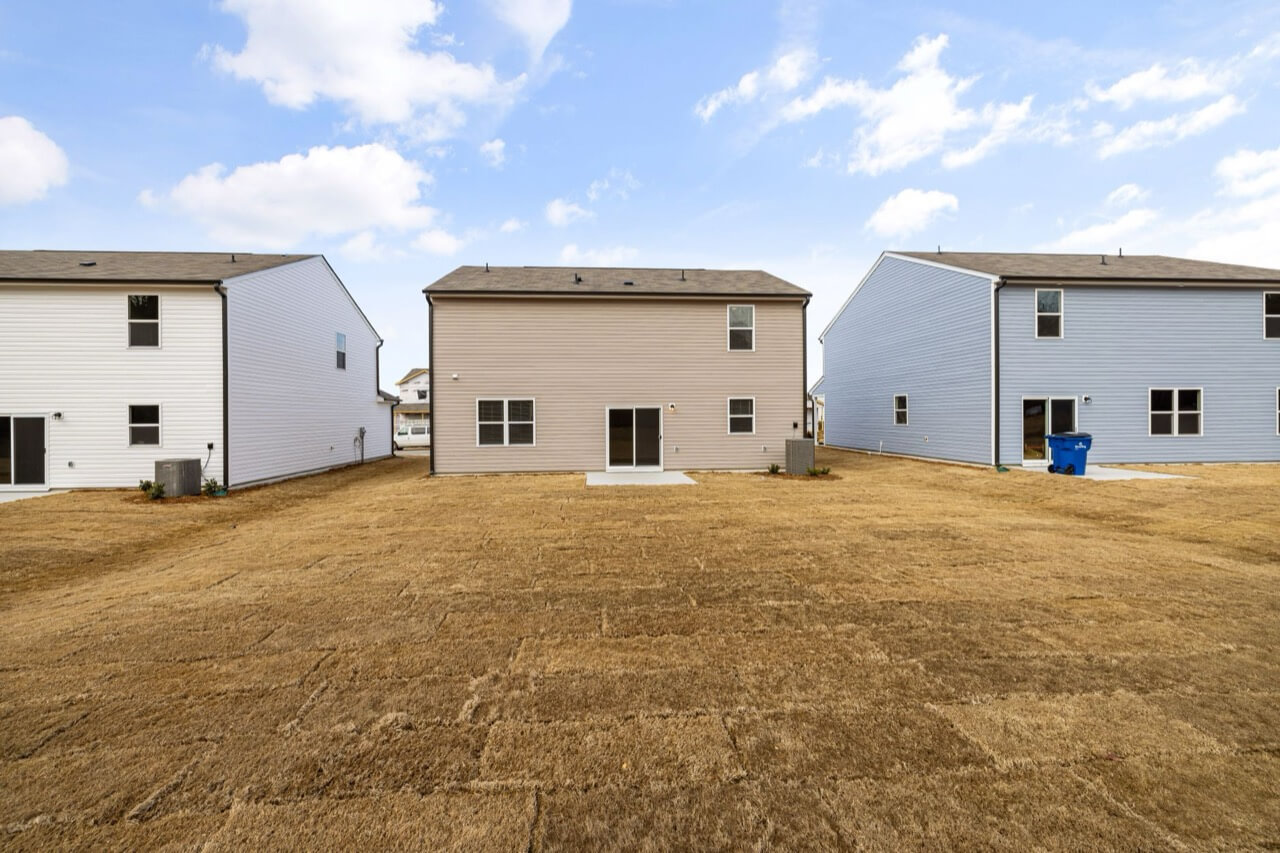 rear view of three newly built suburban houses with vinyl siding under a blue sky