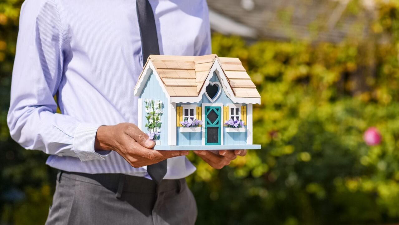 man holding a miniature blue house outdoors