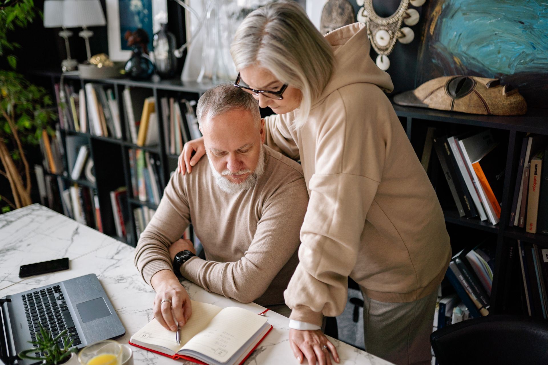An older couple reviewing a notebook together at a desk.