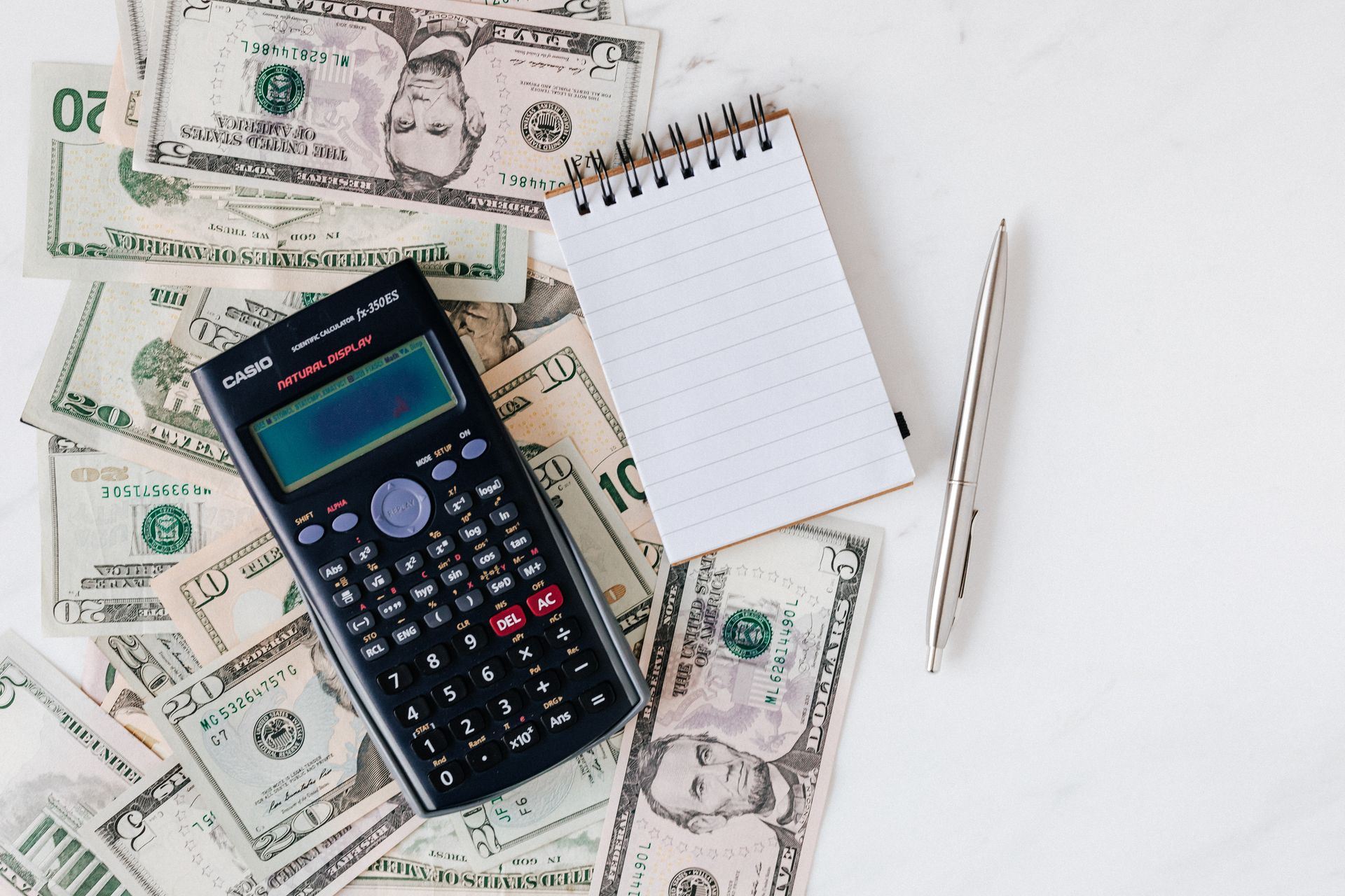 A calculator, notebook, and pen arranged over US dollar bills for budget planning.