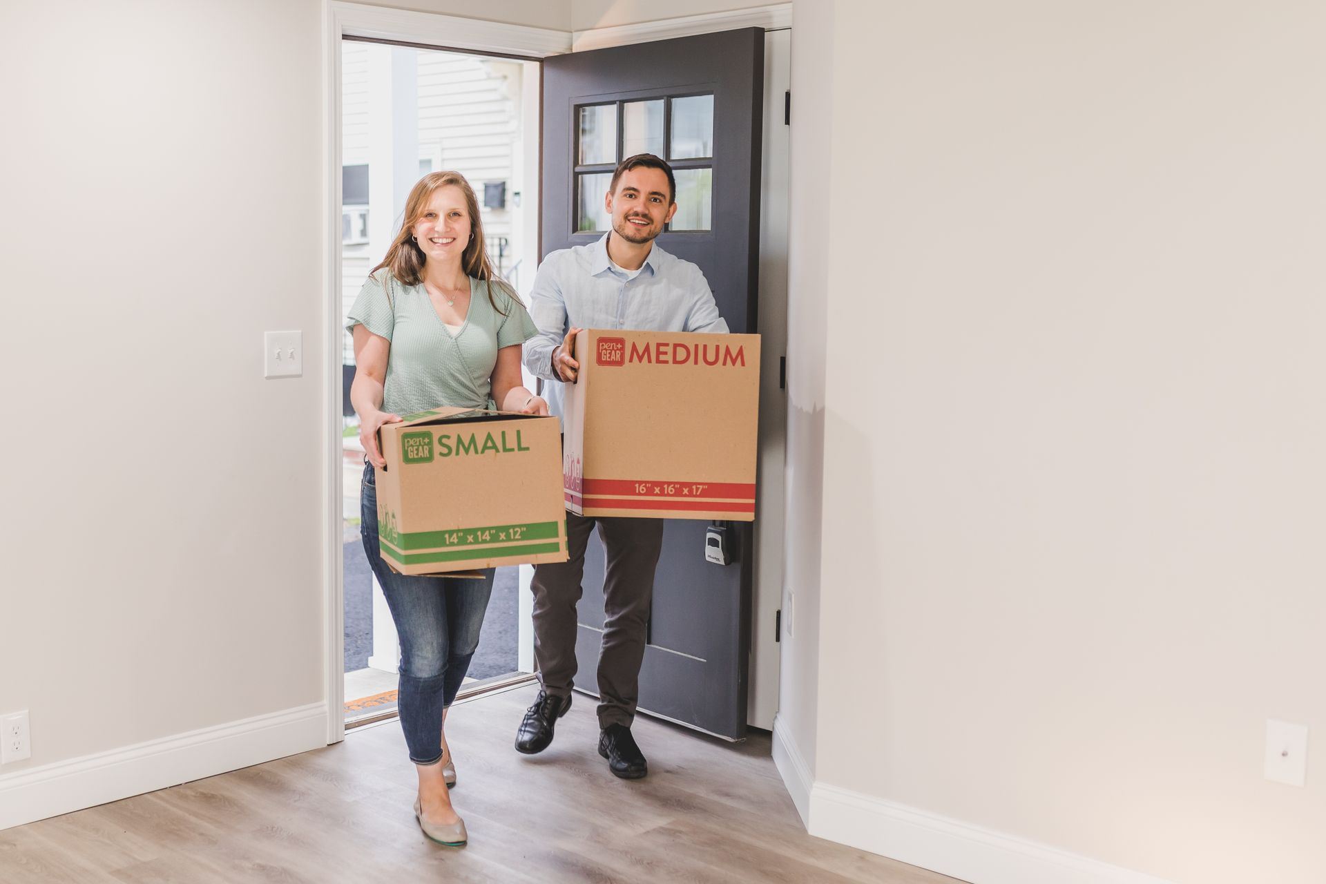A smiling couple carrying cardboard boxes into their new home.