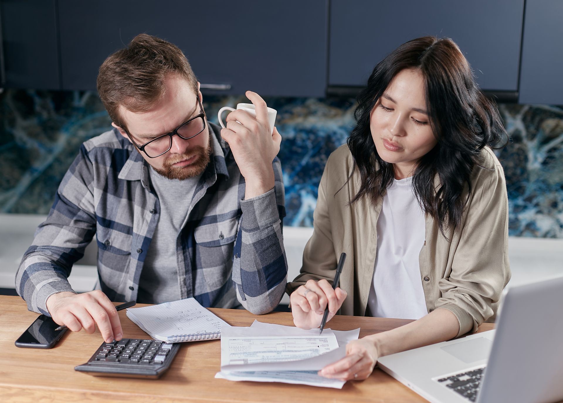 A couple reviewing bills with a calculator and laptop at their kitchen table.