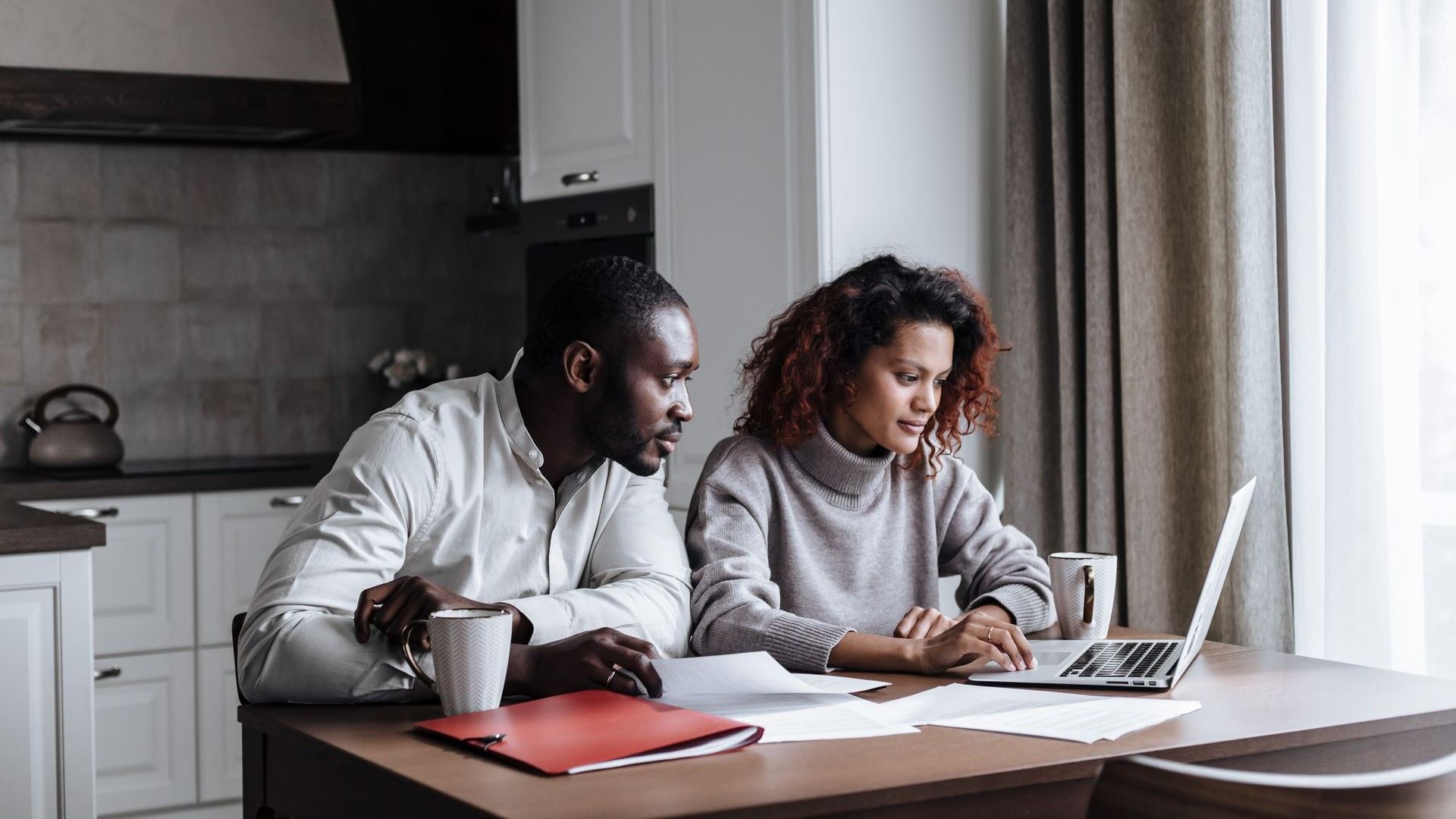 Two people using a laptop together at a kitchen counter.