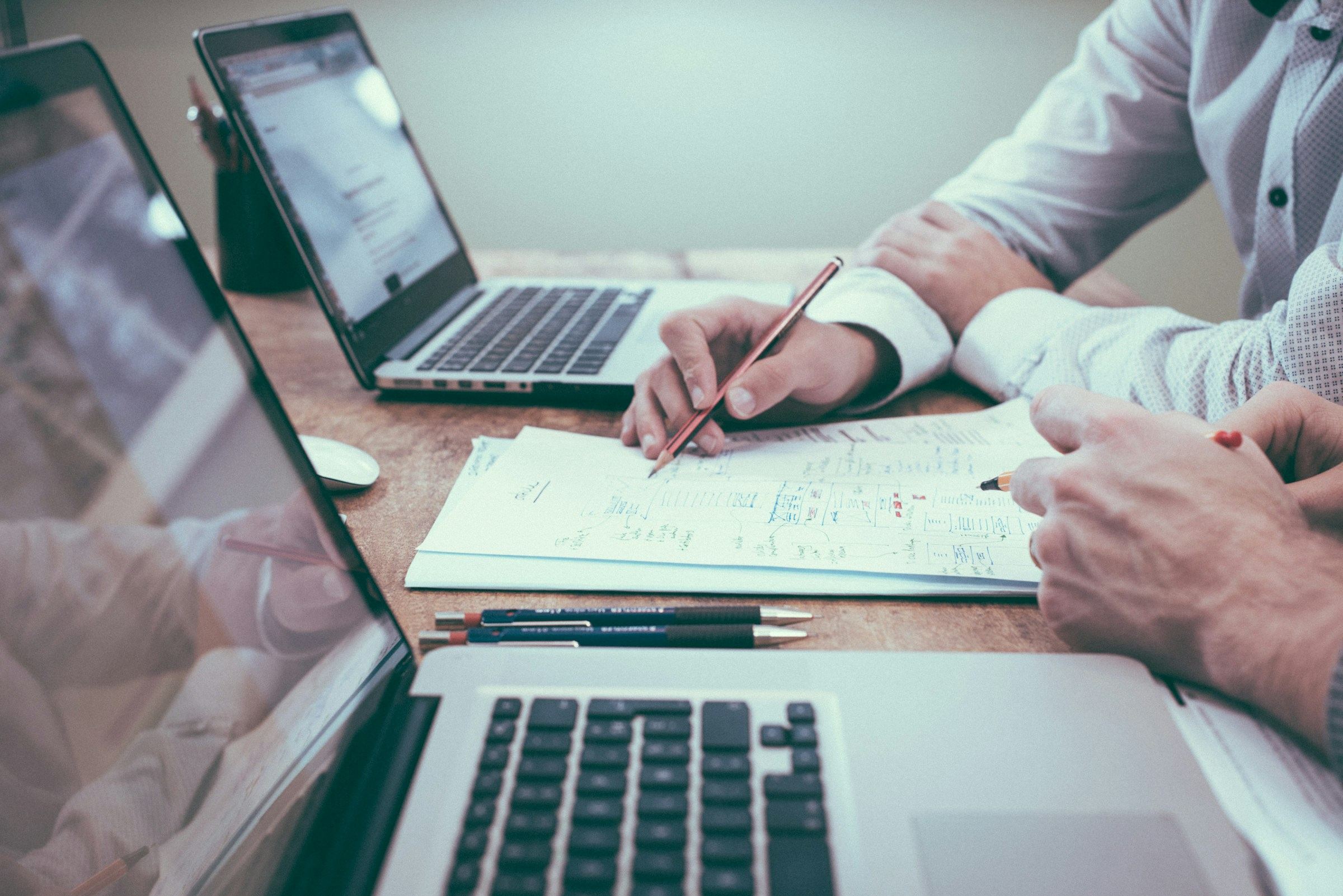 People reviewing paperwork together at a table with laptops.