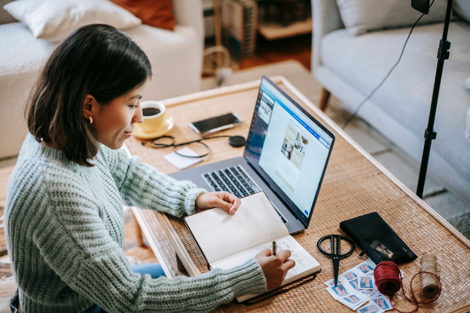 Woman writing in a planner beside an open laptop.