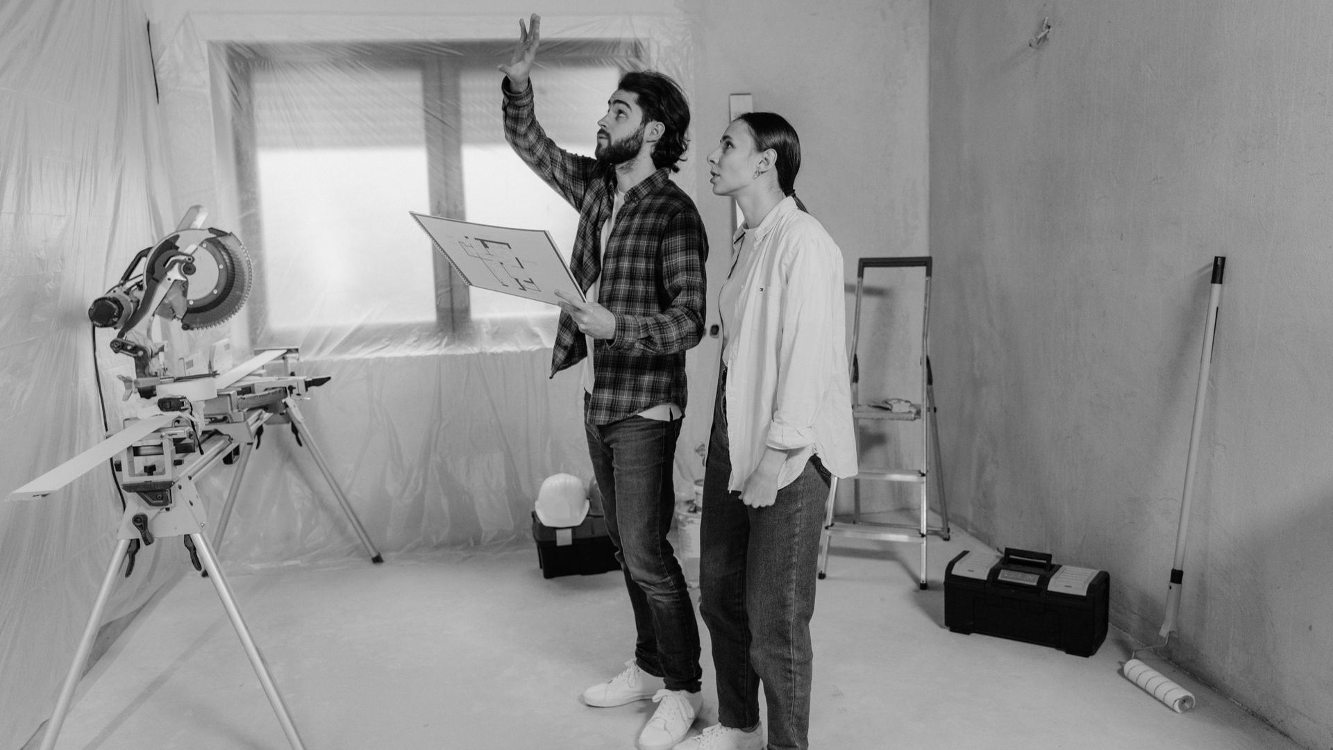 Couple working Couple working on home renovation plans indoors, analyzing blueprints in a construction setting.