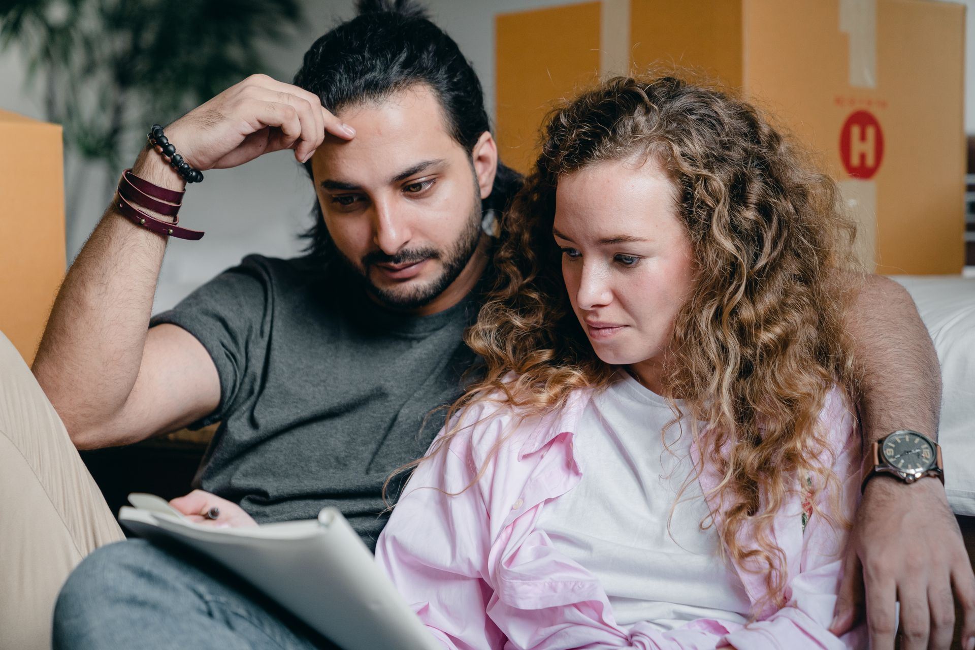 A couple reviewing a notebook together while sitting near moving boxes.
