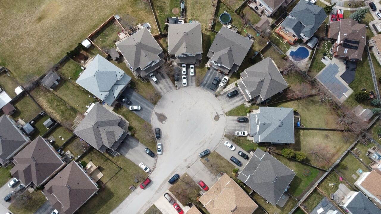 Straight-down aerial view of a suburban cul-de-sac ringed by detached houses with gray and brown shingled roofs